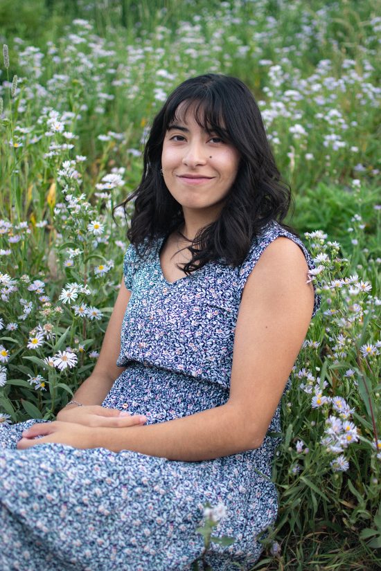 A woman smiling and sitting in a field of wildflowers